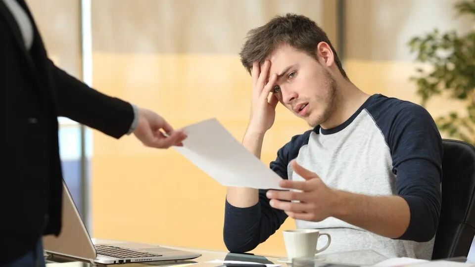 Büromitarbeiter bekommt Zettel mit erschreckender/ niederschmetternder Nachricht von seiner Chefin/ Vorgesetzten überreicht und hält die Hand an seine Stirn.