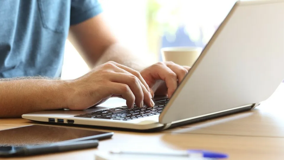 Close up of man hands typing on a laptop keyboard on a desk at home or office