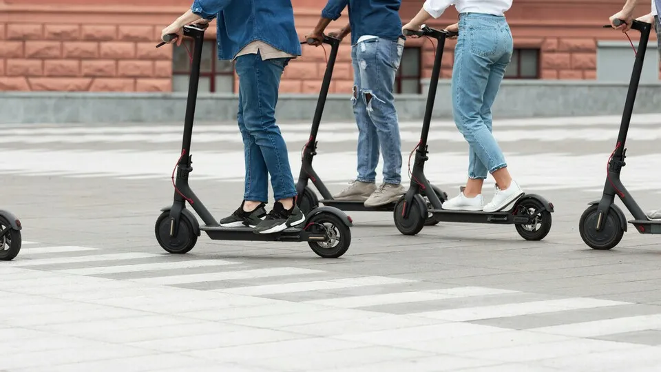 Eine Gruppe aus Frauen und Männern fährt auf ElektroscooternActive Lifestyle. Cropped view of five multiracial millennials driving electric kick scooters in downtown, banner