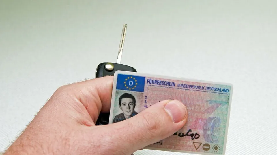 Eine Hand mit einem Autoschlüssel und einem Führerschein.