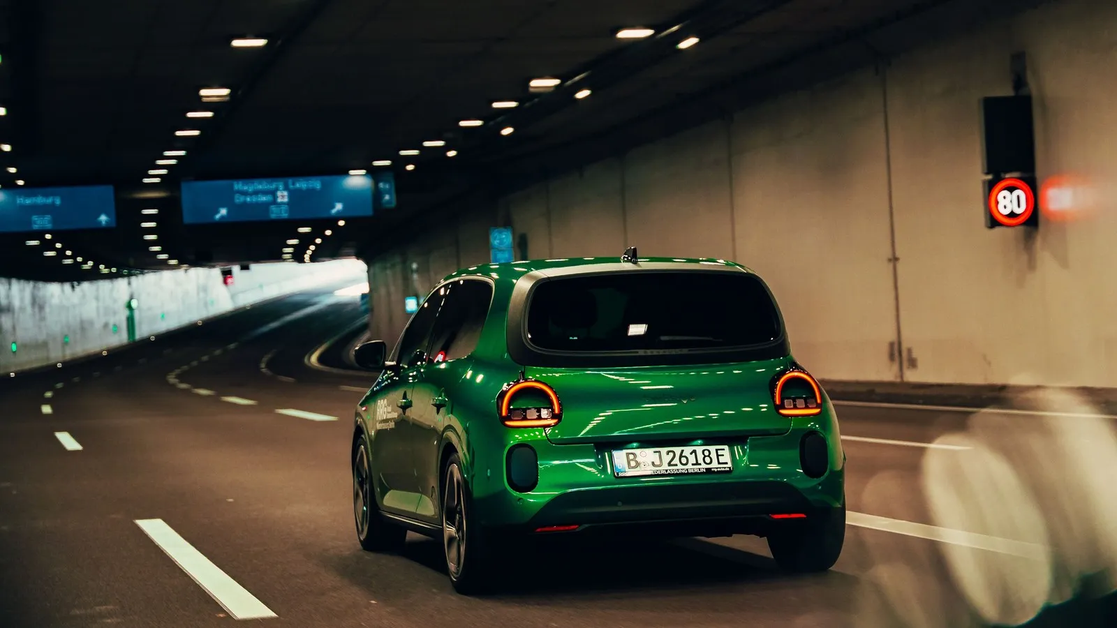 Grüner Renault Twingo Electric fährt von hinten gesehen durch einen beleuchteten Straßentunnel.