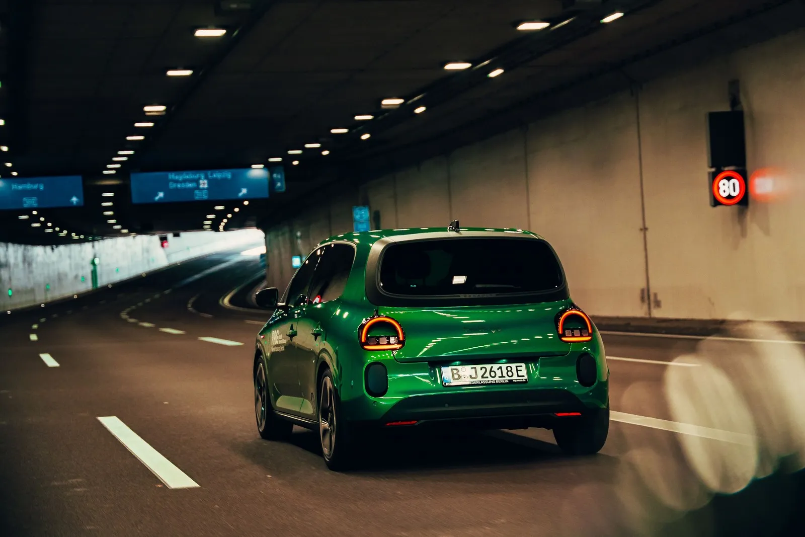 Grüner Renault Twingo Electric fährt von hinten gesehen durch einen beleuchteten Straßentunnel.