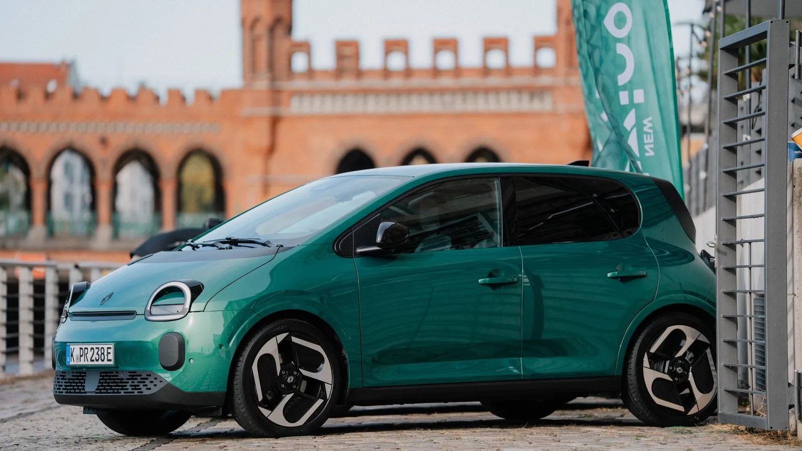 Grüner Renault Twingo Electric in Seitenansicht, geparkt auf einer gepflasterten Fläche.