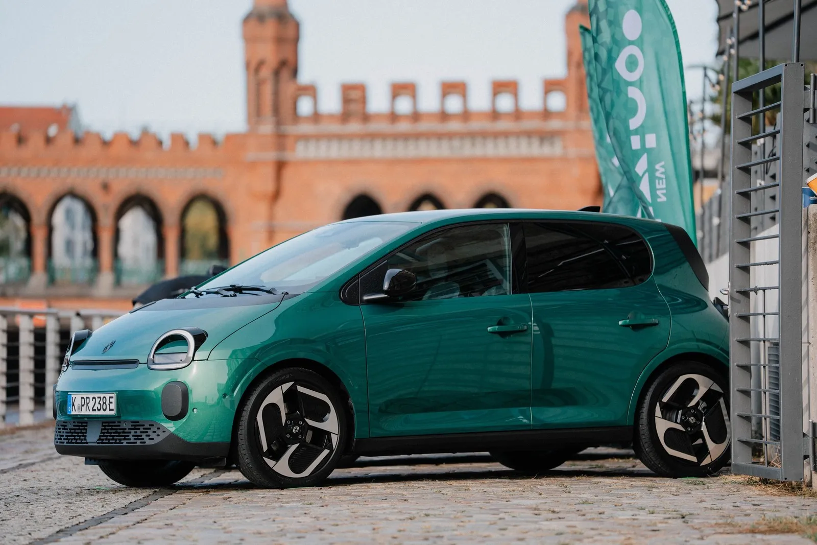 Grüner Renault Twingo Electric in Seitenansicht, geparkt auf einer gepflasterten Fläche.
