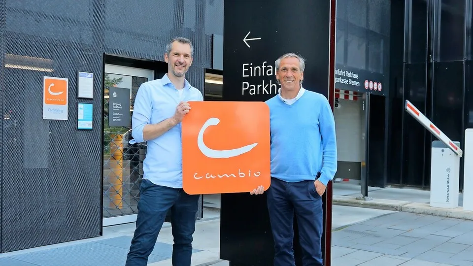 Lasse Schulz von cambio (links) und Michael Hilbers von der Sparkasse Bremen stehen vor der Einfahrt zum Parkhaus der Sparkassen-Zentrale in Bremen, in dem die cambio-Station zu finden ist.