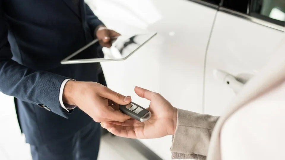 Autoverkäufer übergibt Schlüssel
High angle close up of car salesman giving keys to client standing next to white luxury car, copy space