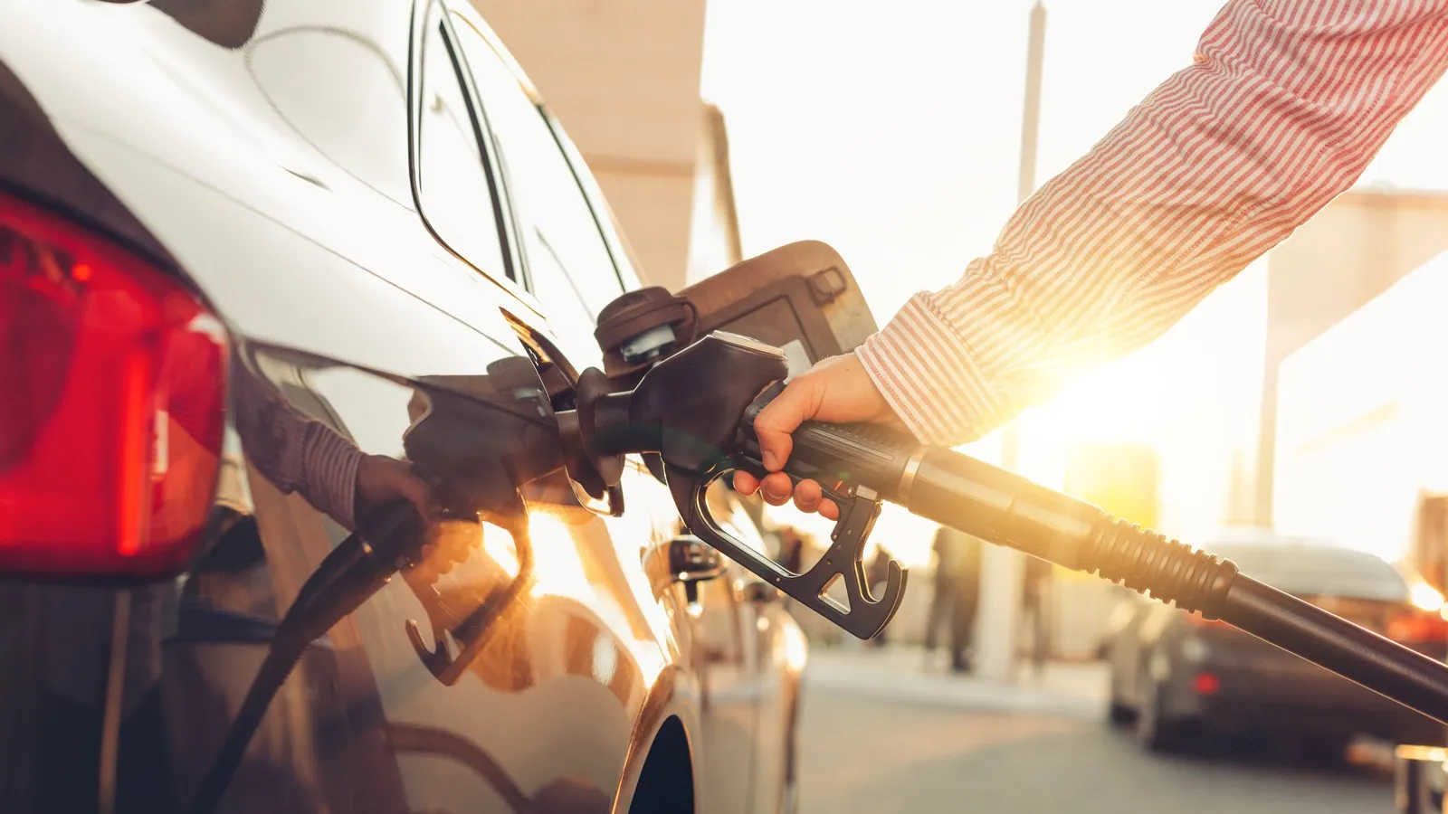 Eine Person dein Auto an einer Tankstelle bei Sonnenschein.