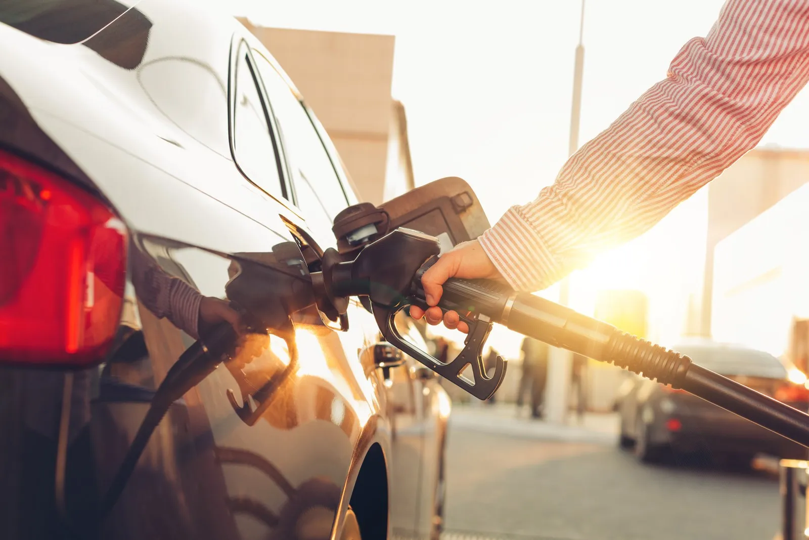 Eine Person dein Auto an einer Tankstelle bei Sonnenschein.